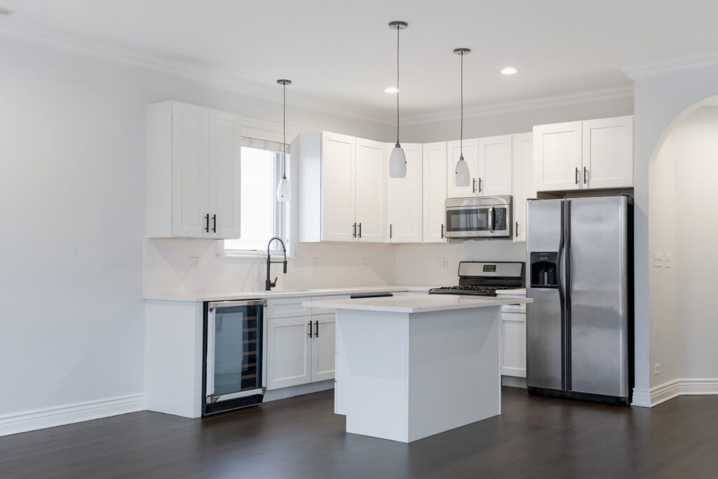 Finished white kitchen with an island, pendant lighting and dark hardwood flooring
