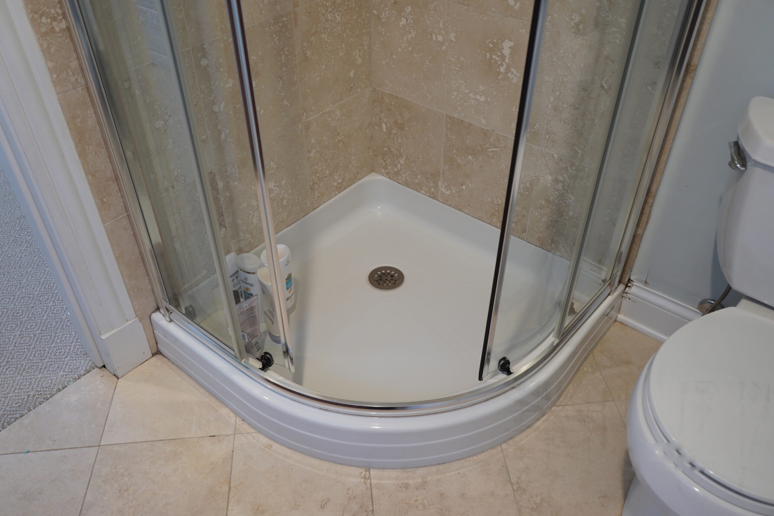 Corner shower enclosure with curved glass doors and a white shower base
