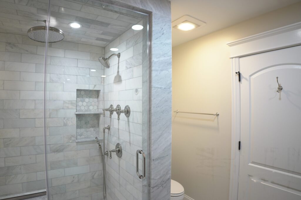 Marble subway tiled shower with a recessed niche, rainfall head and a frameless glass door