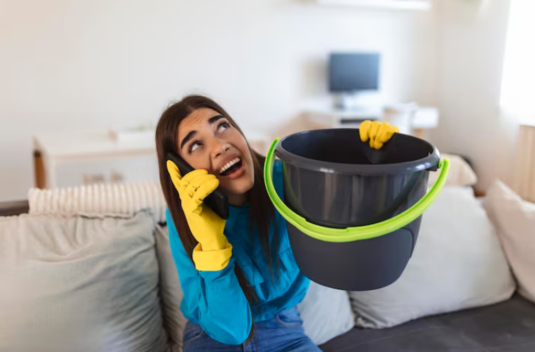 Woman holding a bucket and talking on the phone while wearing cleaning gloves