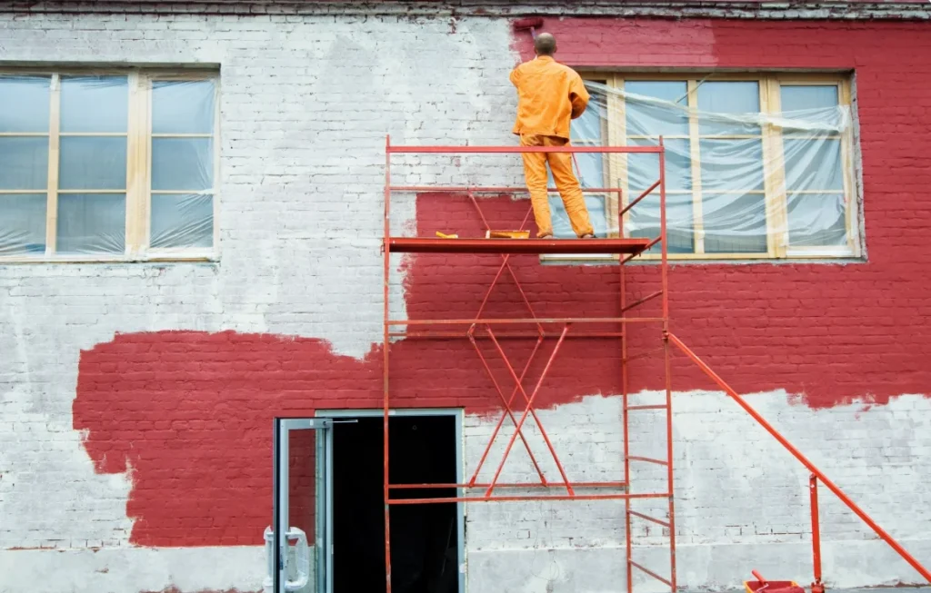 Painter on a scaffold cutting a clean edge on a painted brick exterior